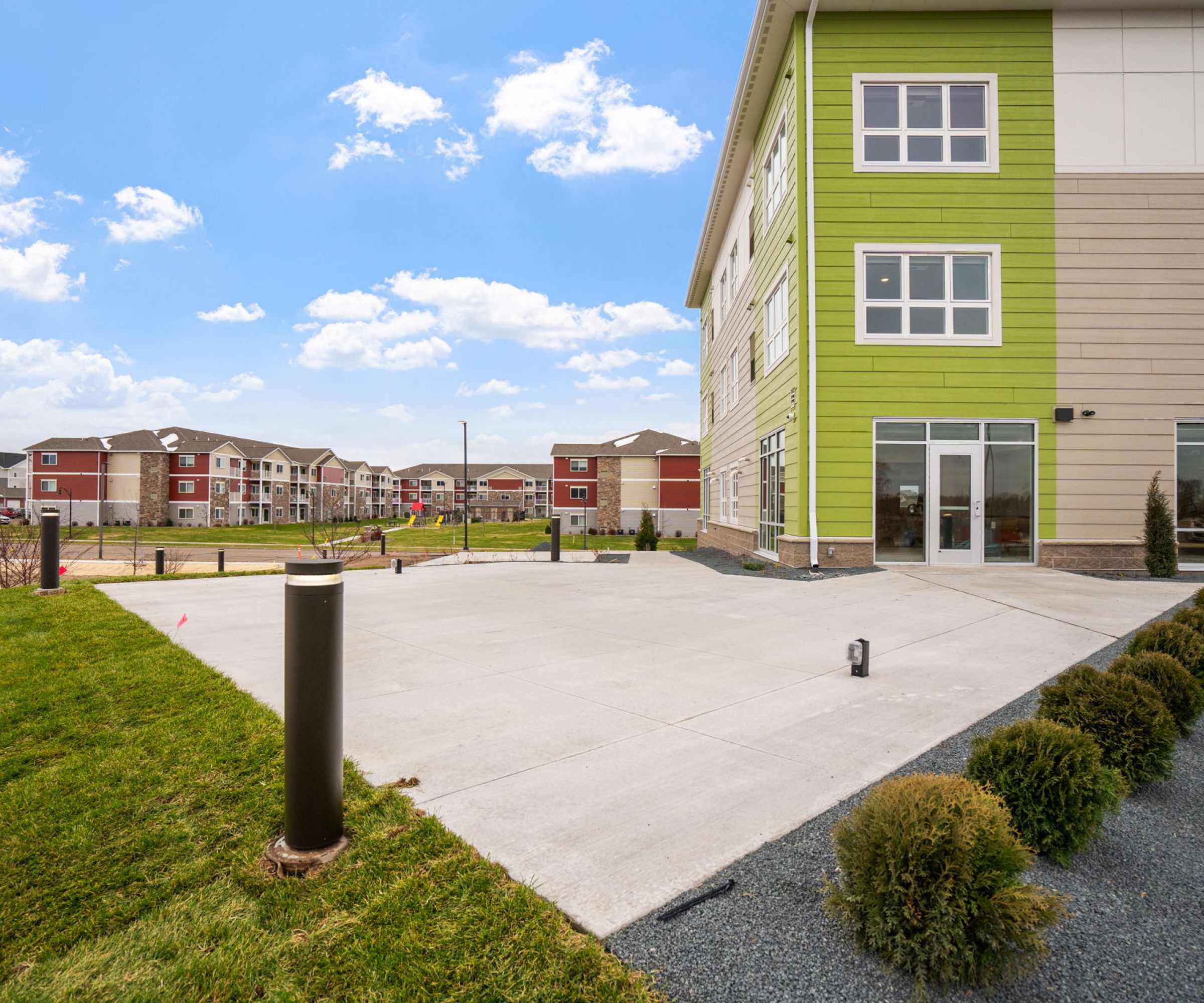 Aeon Affordable Homes and Community Affordable apartment homes featuring green accents, large windows, and landscaped surroundings under a blue sky.