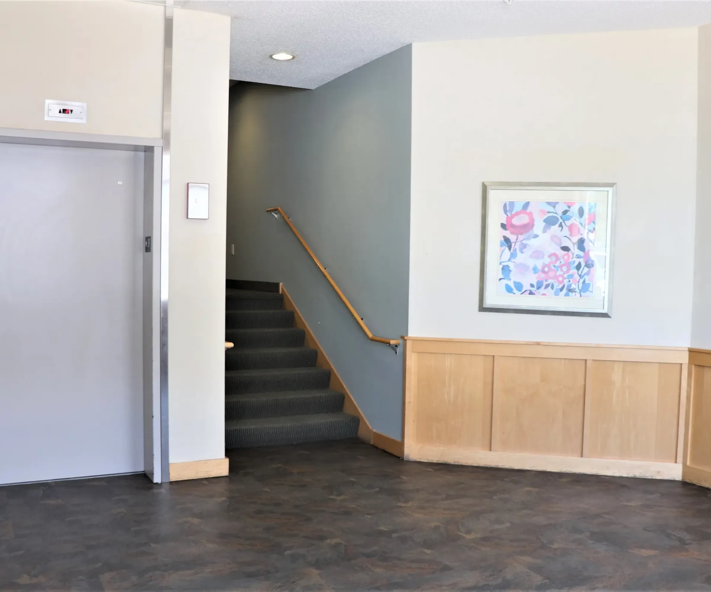 Aeon Affordable Homes and Community Lobby of affordable apartment homes with elevator doors on the left, stairs in the middle, and a floral painting on a light gray wall.