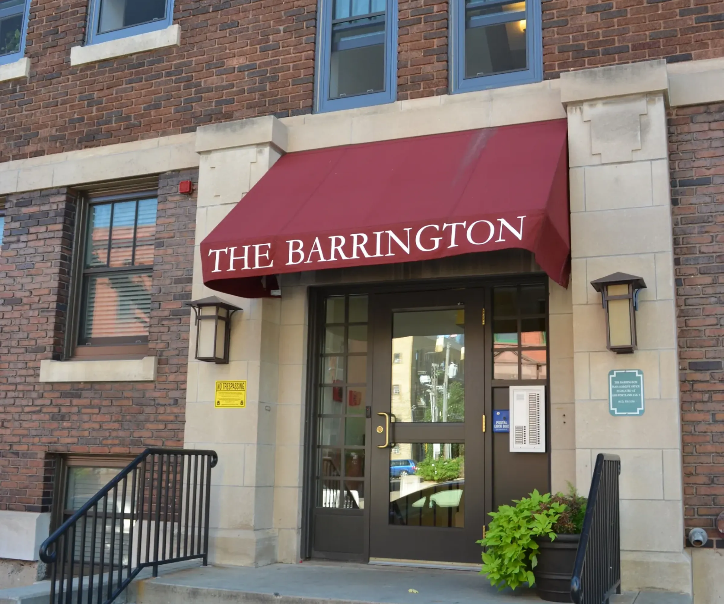 Aeon Affordable Homes and Community Entrance of a brick building with "The Barrington" on a red awning, leading to affordable apartment homes up the steps.