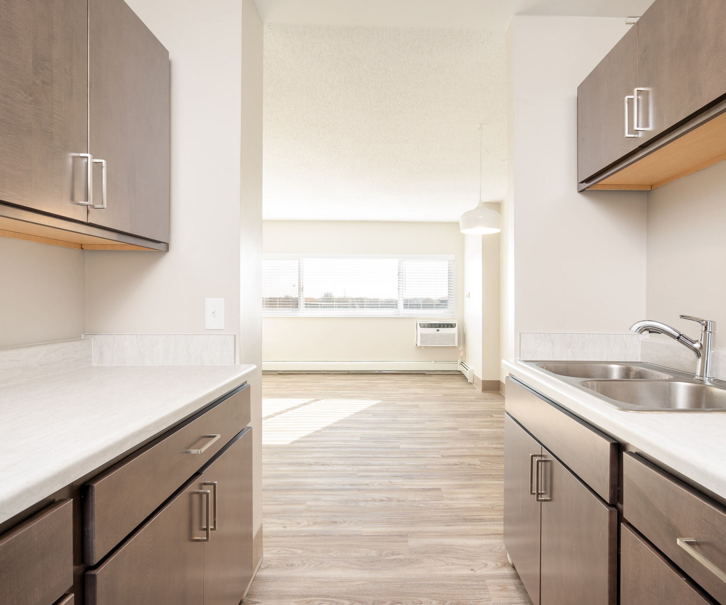 Aeon Affordable Homes and Community Affordable apartment homes featuring a modern kitchen with dark wood cabinets, light countertops, and a view into a bright living room with large windows.