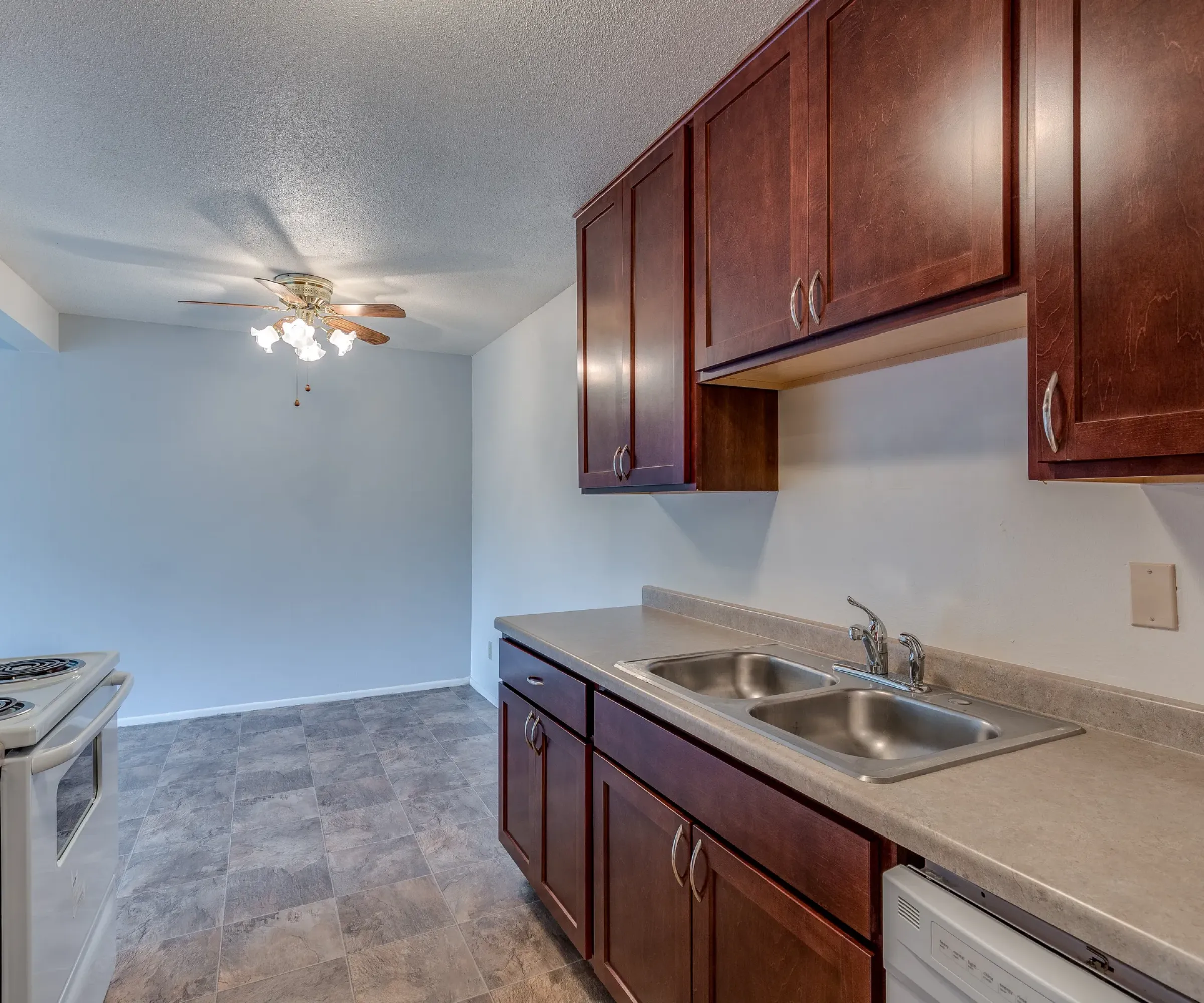 Aeon Affordable Homes and Community Affordable apartment homes featuring a kitchen with brown cabinets, double sink, stove, tile flooring, and dining area ceiling fan with lights.