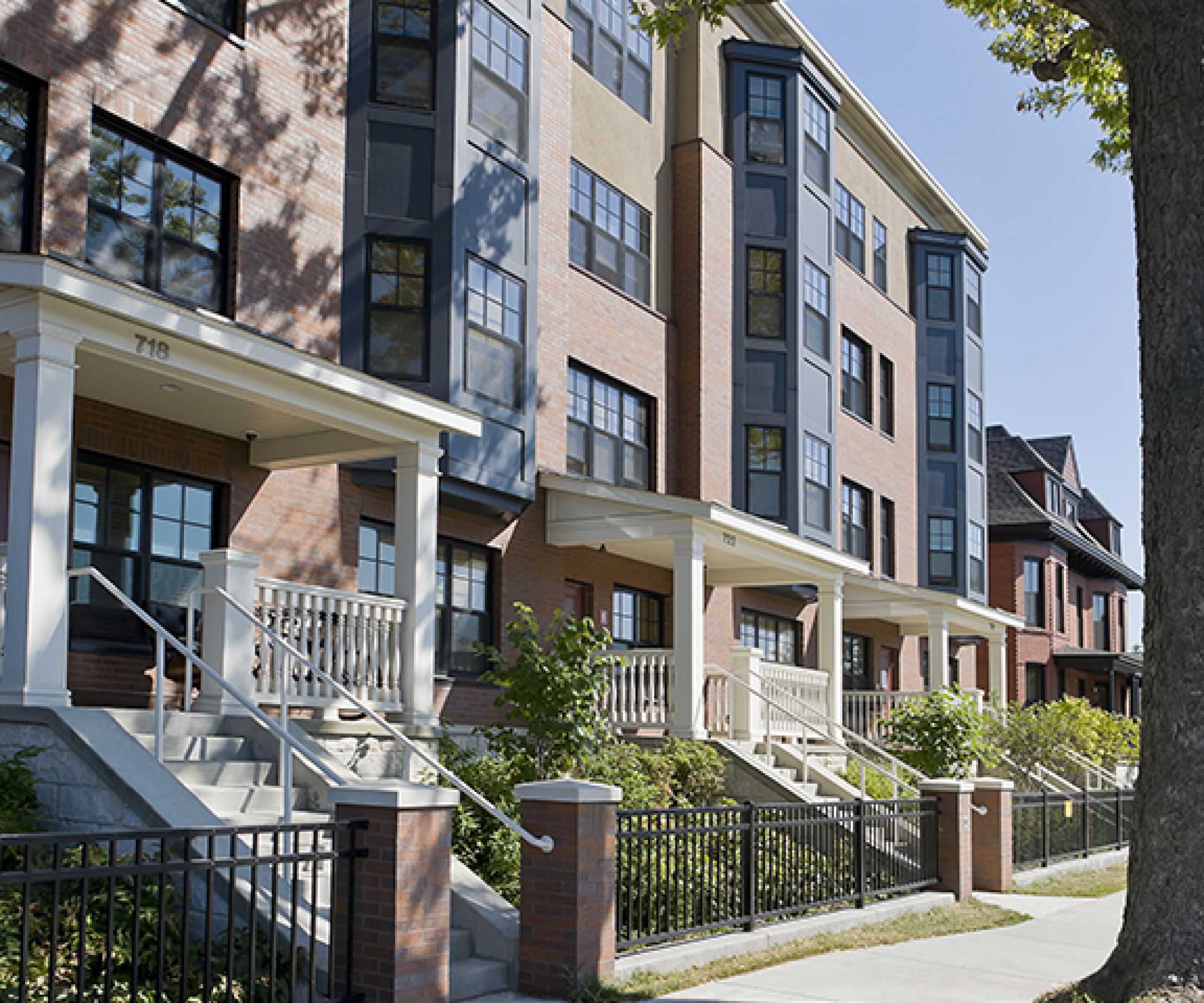 Aeon Affordable Homes and Community Tree-lined sidewalk in front of modern brick townhouses with large windows and balconies offers affordable apartment homes.