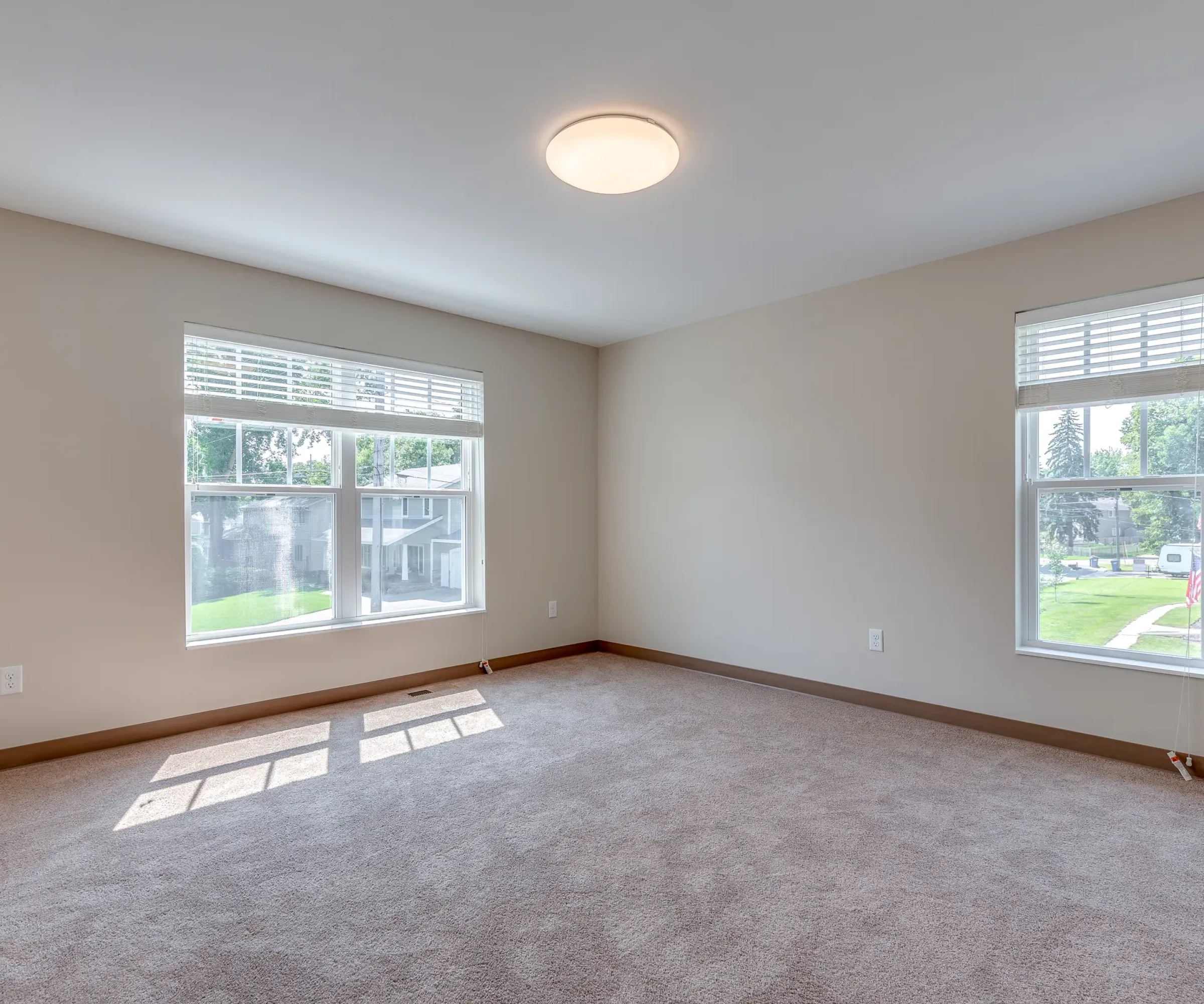Aeon Affordable Homes and Community Affordable apartment homes featuring an empty room with beige carpet, two windows overlooking green trees and a circular ceiling light.
