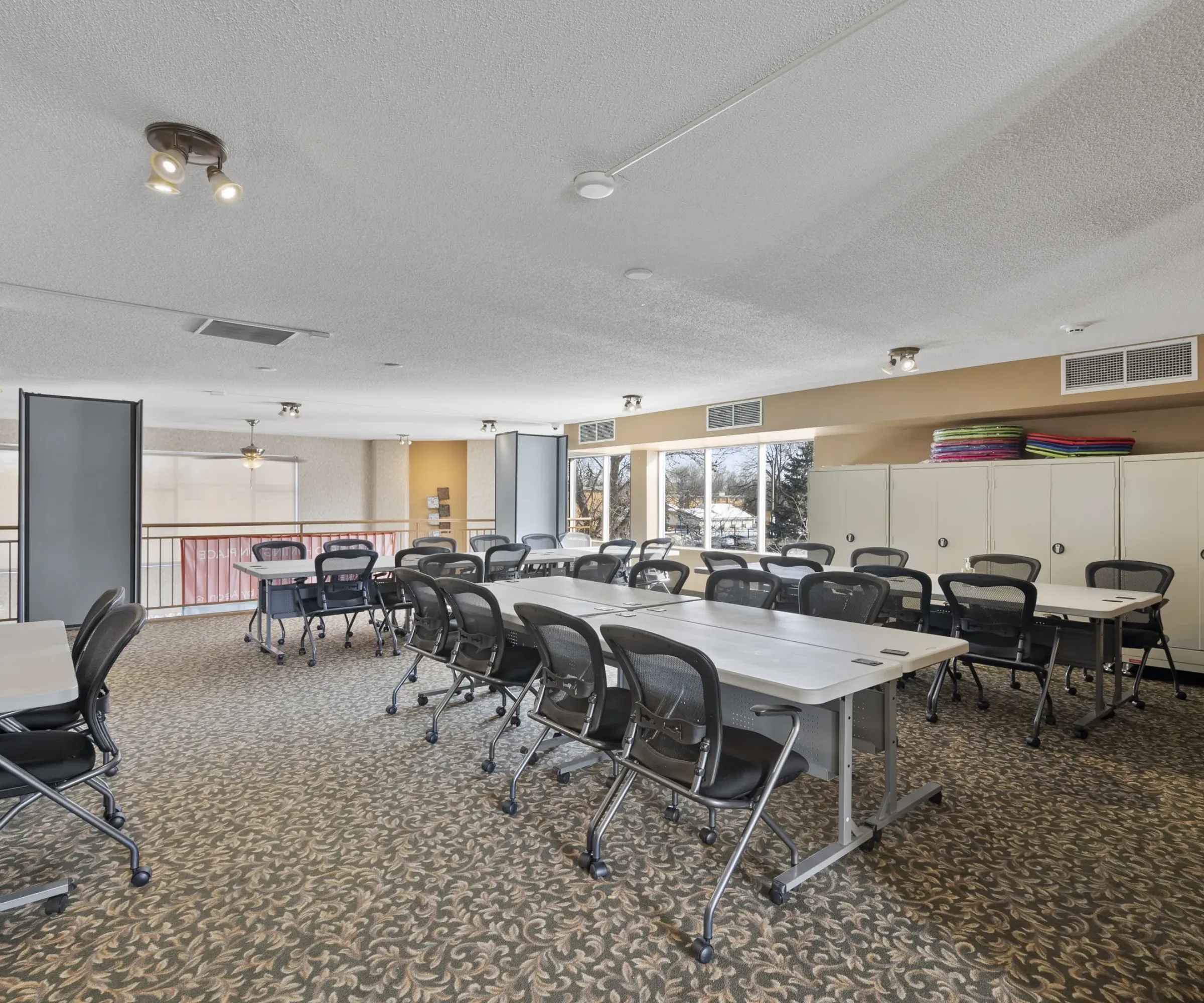 Aeon Affordable Homes A classroom with tables, chairs, cabinets, and large windows overlooking a snowy scene outside.