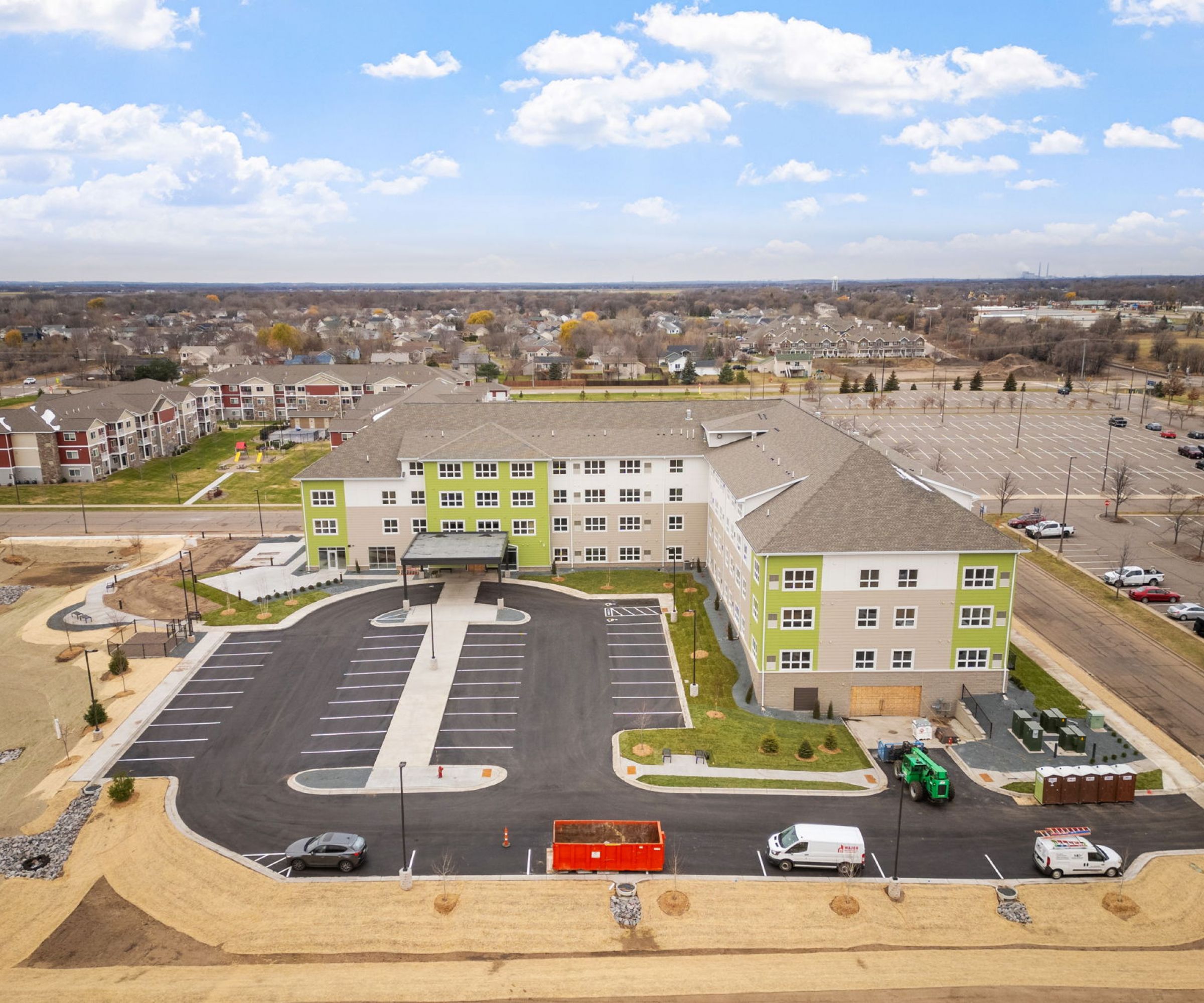 Aeon Affordable Homes and Community Aerial view of affordable apartment homes in a large, rectangular building with a parking lot, surrounded by roads and open land.