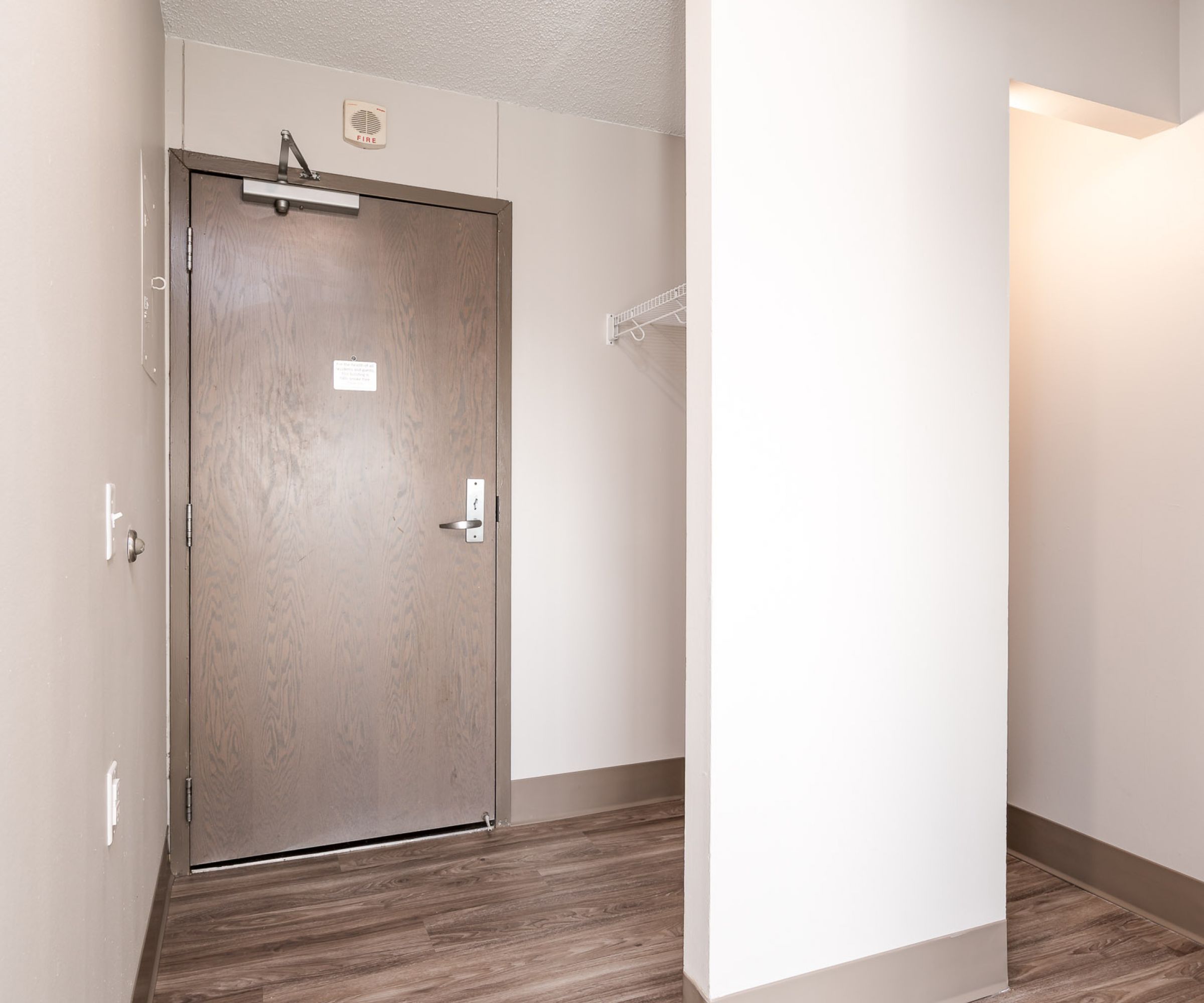 Aeon Affordable Homes and Community Affordable apartment homes featuring an empty room with light wood flooring, white walls, a brown door, and a small closet space with a shelf.
