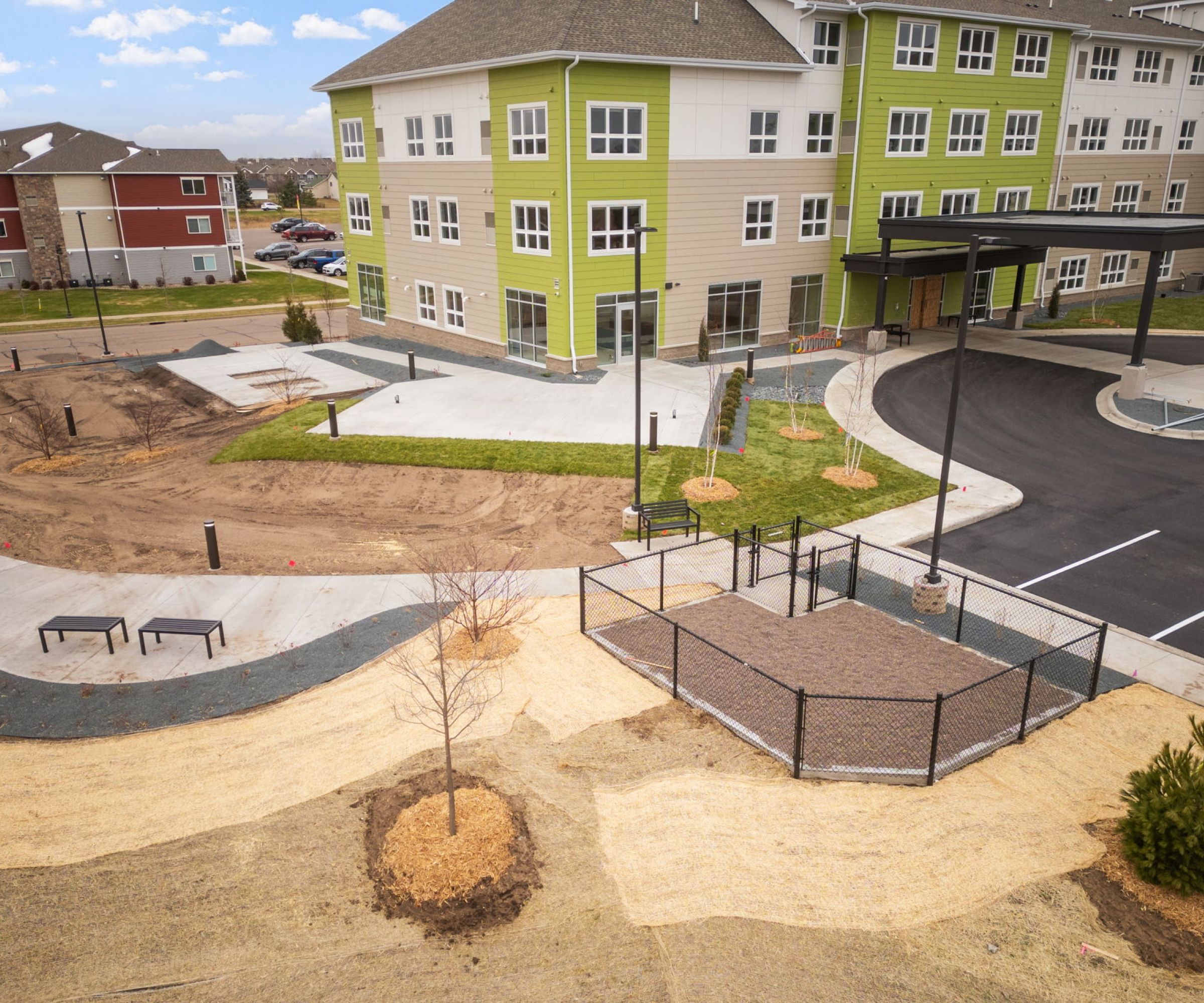 Aeon Affordable Homes and Community Modern apartment building with green accents, affordable apartment homes, adjacent parking area, newly landscaped grounds, and walking paths.
