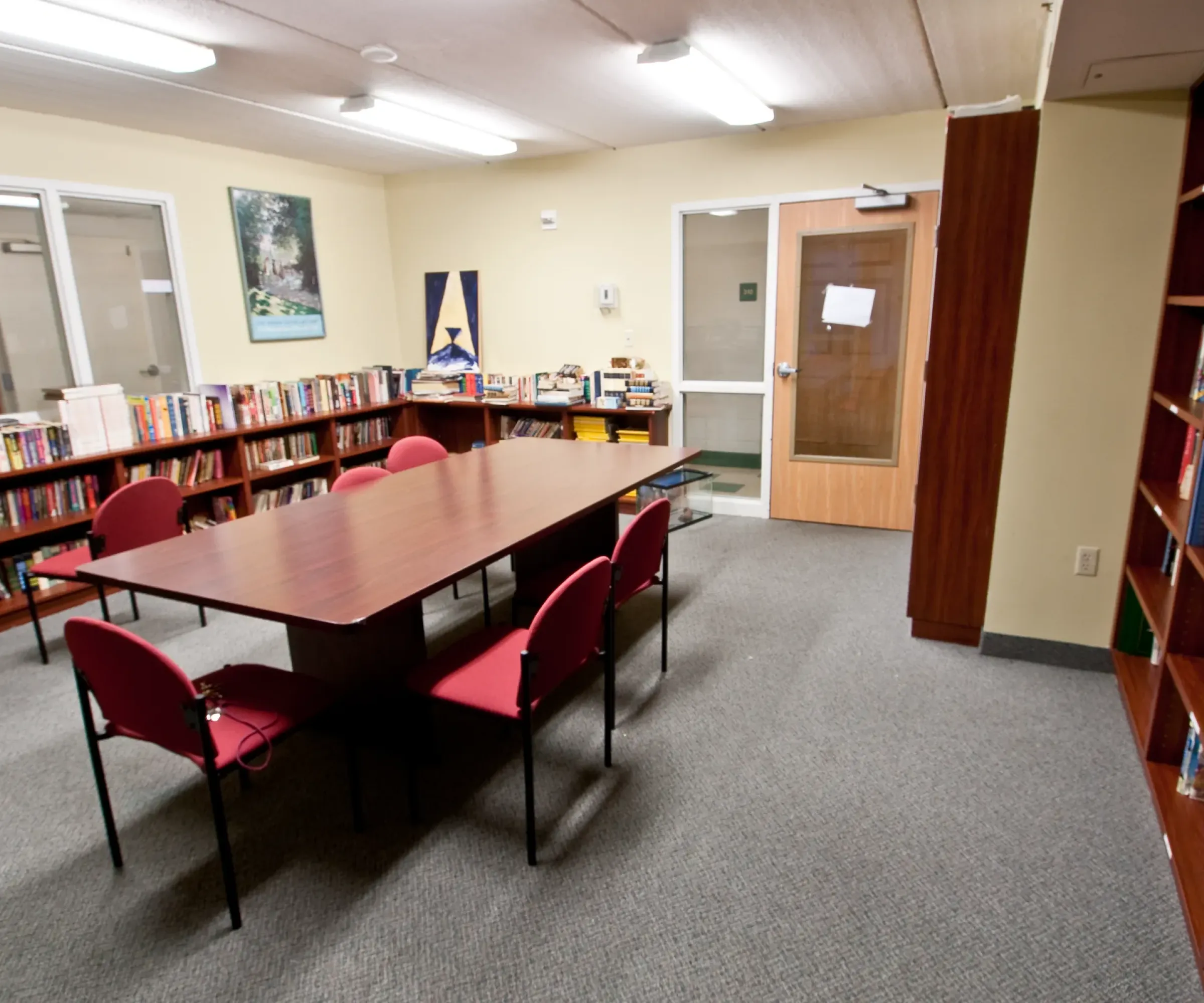 Aeon Affordable Homes and Community Library room in affordable apartment homes with a long table, red chairs, bookshelves, and a glass door welcoming natural light.