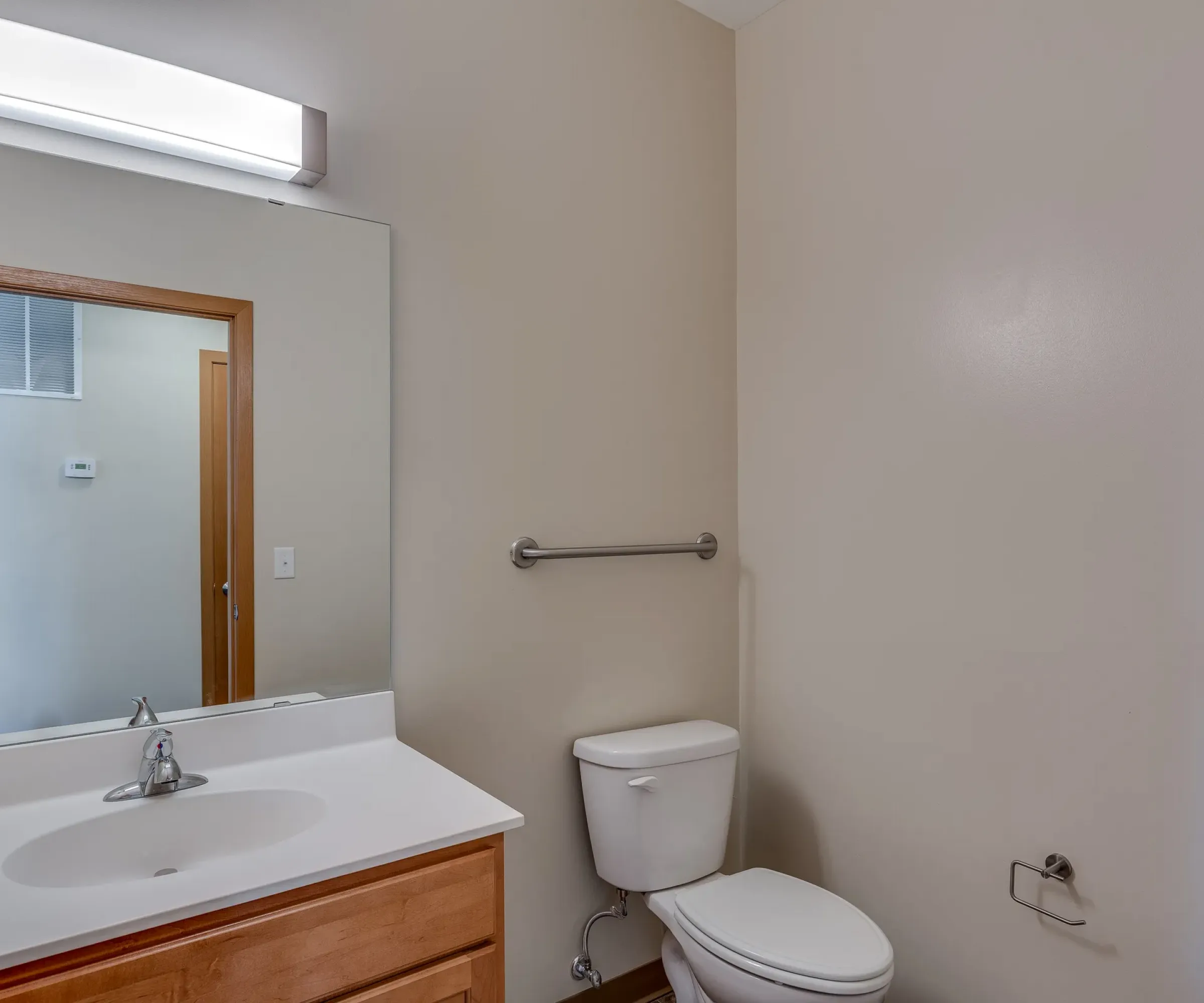 Aeon Affordable Homes and Community Small bathroom in affordable apartment homes with a sink, mirror, toilet, and grab bar on beige walls.