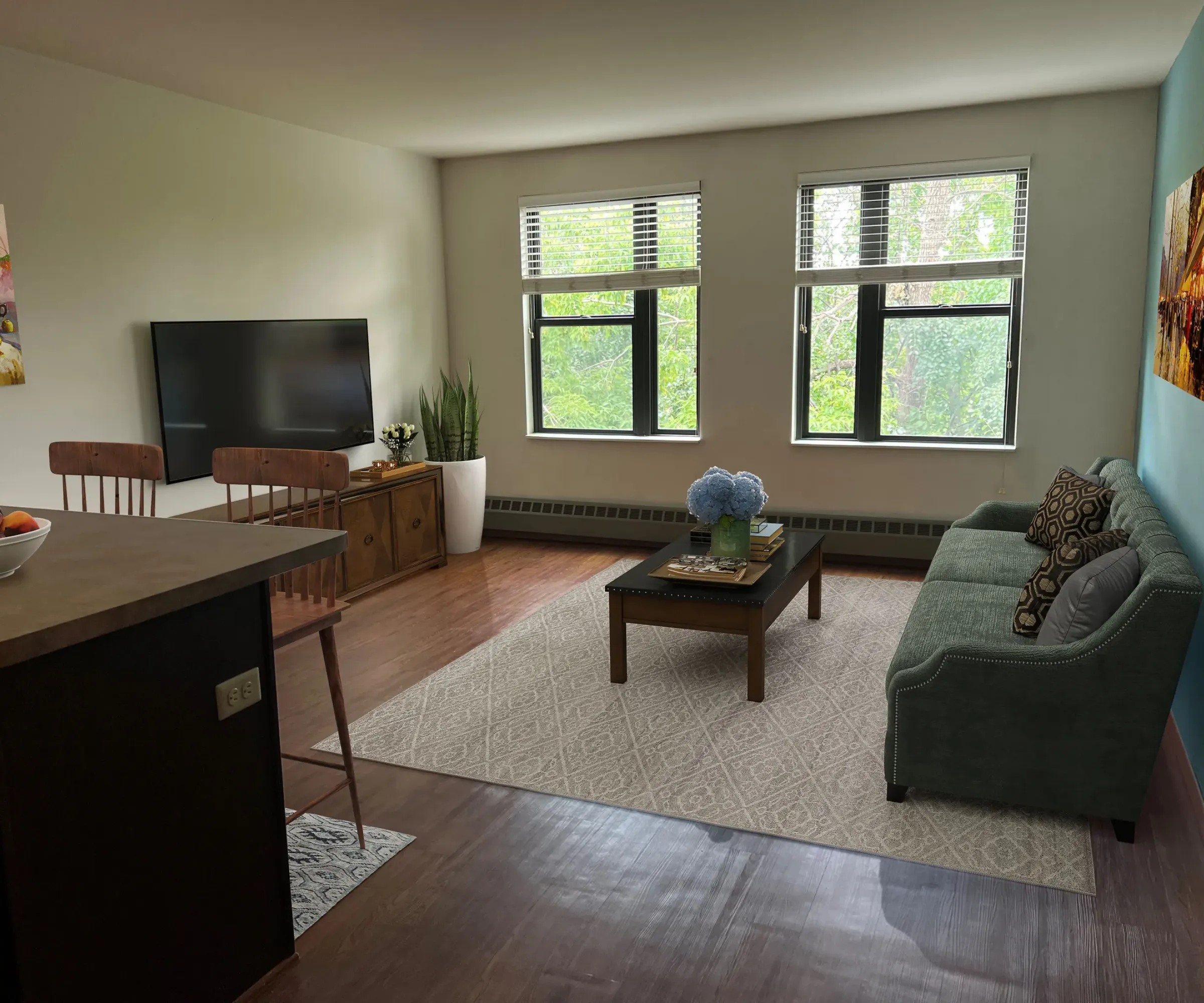 Aeon Affordable Homes and Community Cozy living room in affordable apartment homes with a blue sofa, coffee table, wall-mounted TV, and large windows showcasing trees outside.