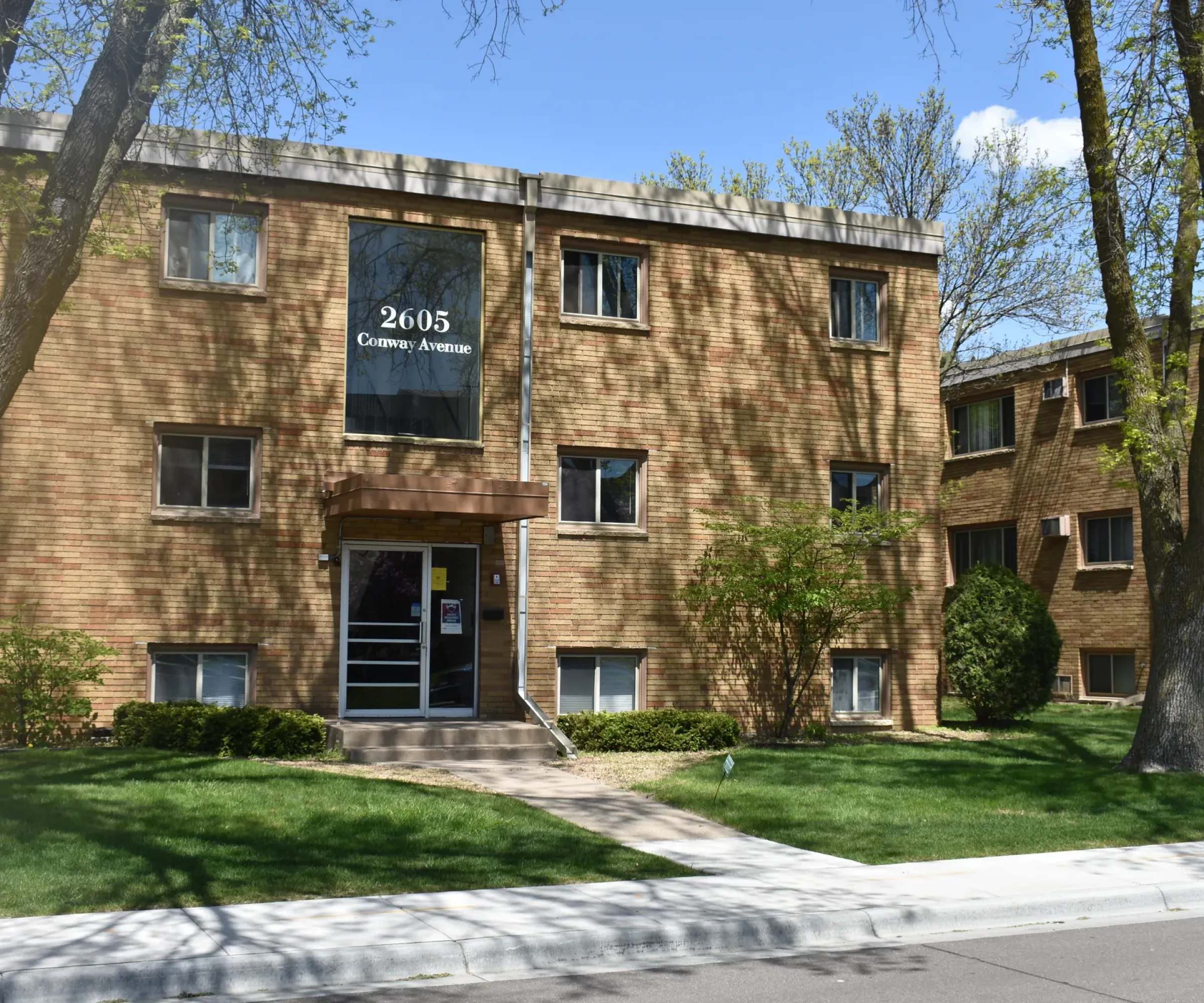 Aeon Affordable Homes The Cobblestone Court Apartments boast a three-story brick design, surrounded by a lush lawn and towering trees.