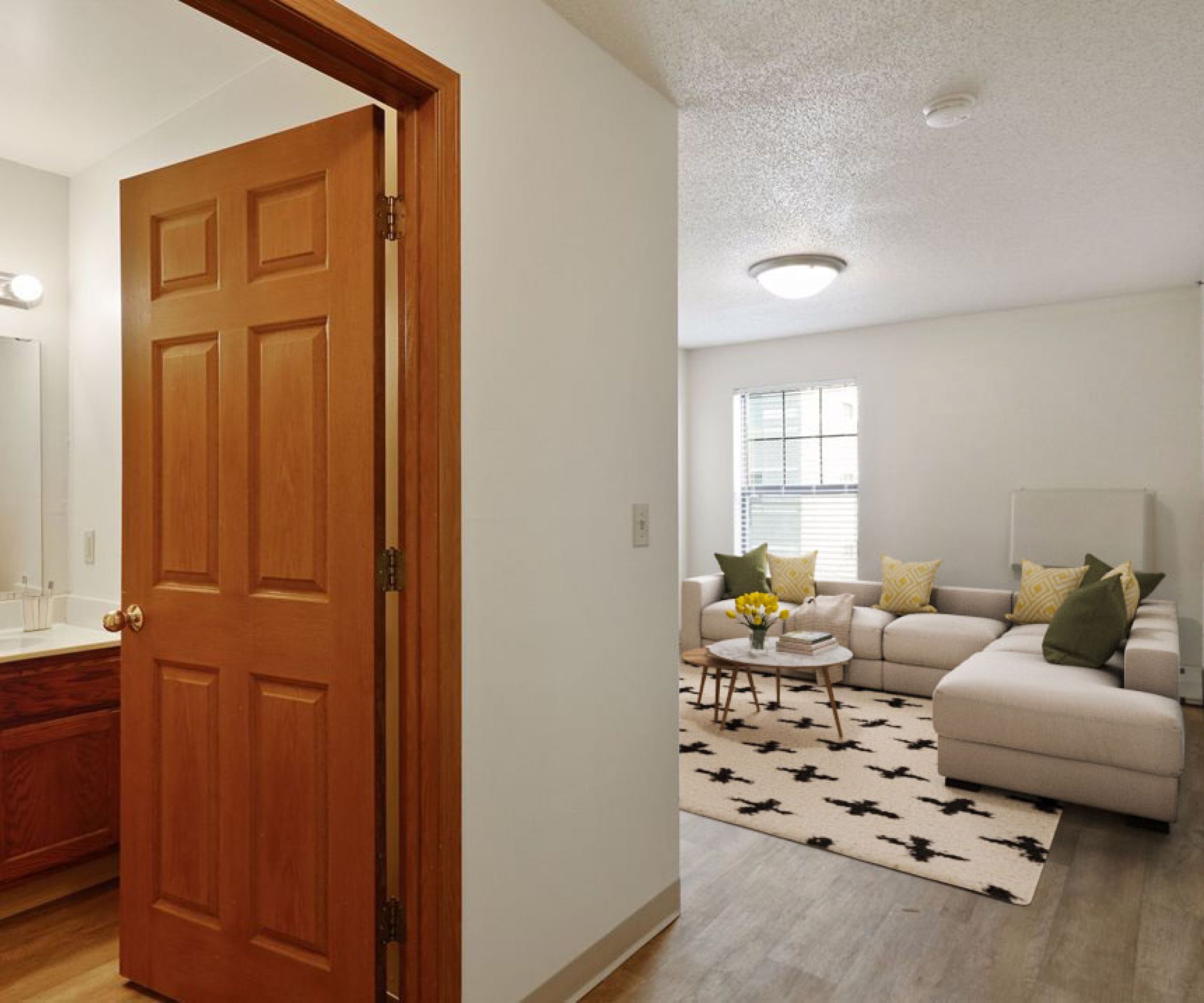 Aeon Affordable Homes and Community Living room with beige sectional sofa, patterned rug, and adjacent bathroom in these affordable apartment homes.