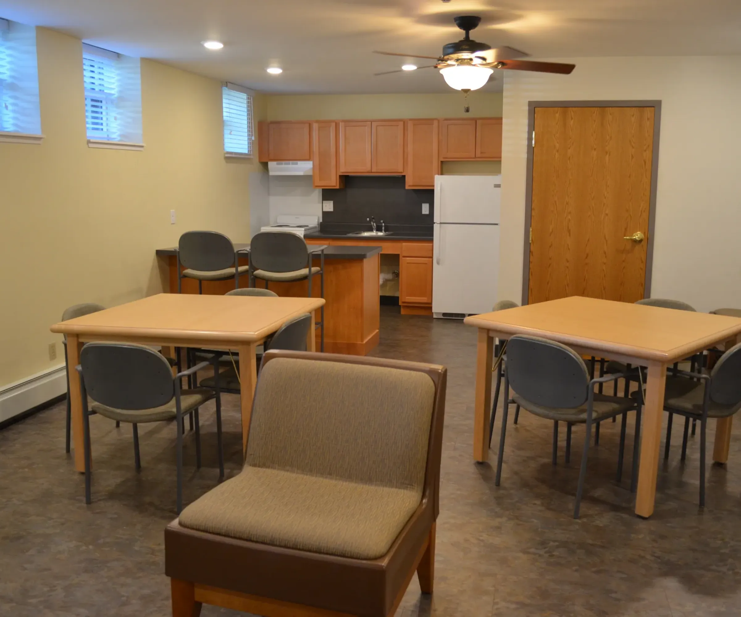 Aeon Affordable Homes and Community Affordable apartment homes with a room featuring tables, chairs, a kitchenette, fridge, ceiling fan, beige walls, and tiled floor.