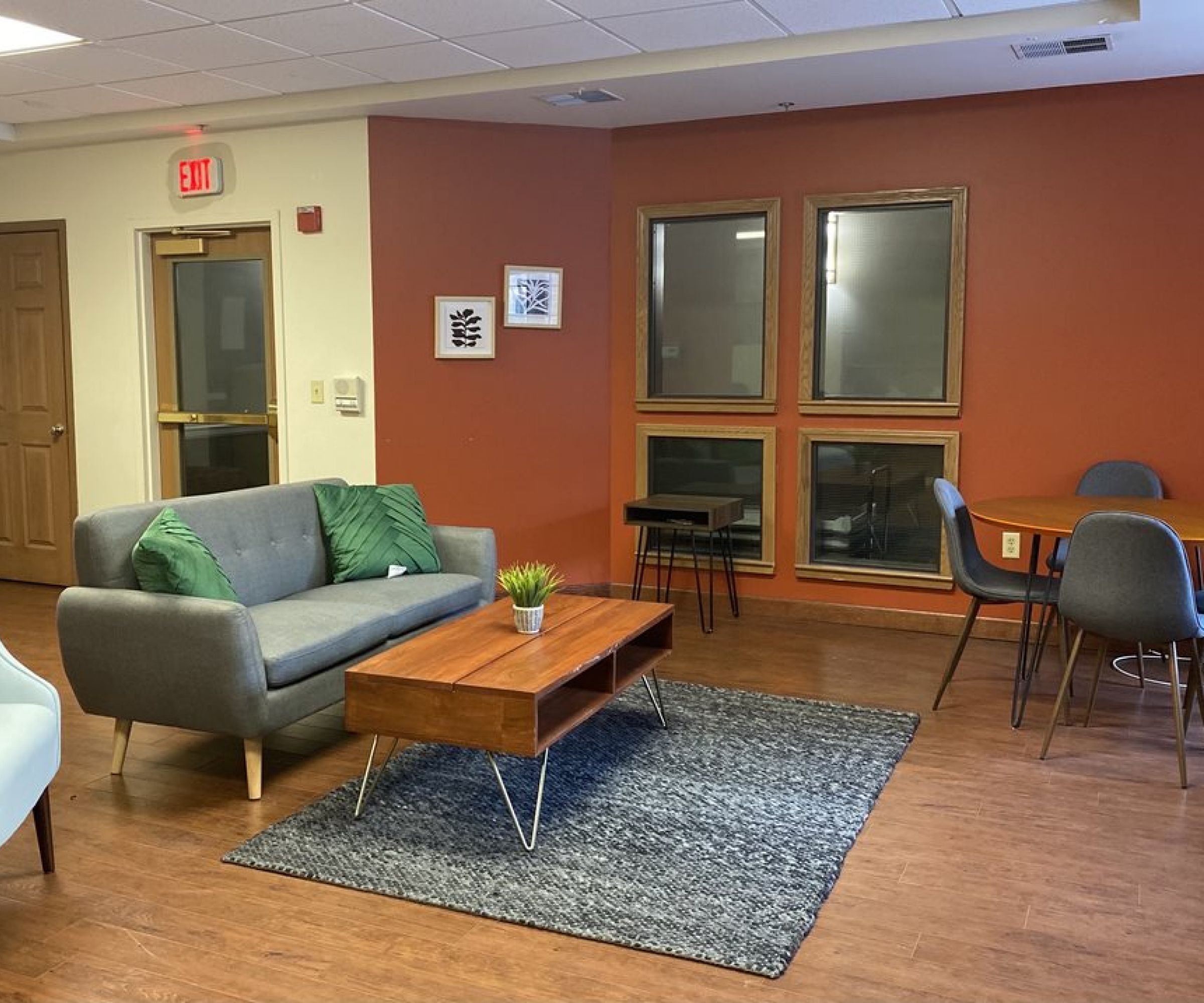 Aeon Affordable Homes and Community A cozy room in affordable apartment homes, featuring a gray sofa, wooden coffee table, and round dining table on hardwood floors.