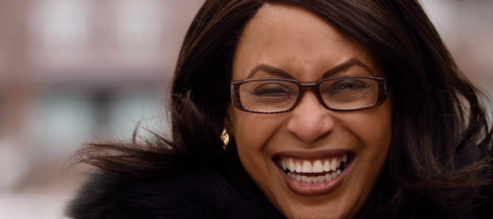 Aeon Affordable Homes and Community A person with glasses smiling brightly and wearing a black coat.