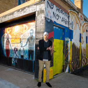 Aeon Affordable Homes resident Matthew in front of a building exterior showcasing his art