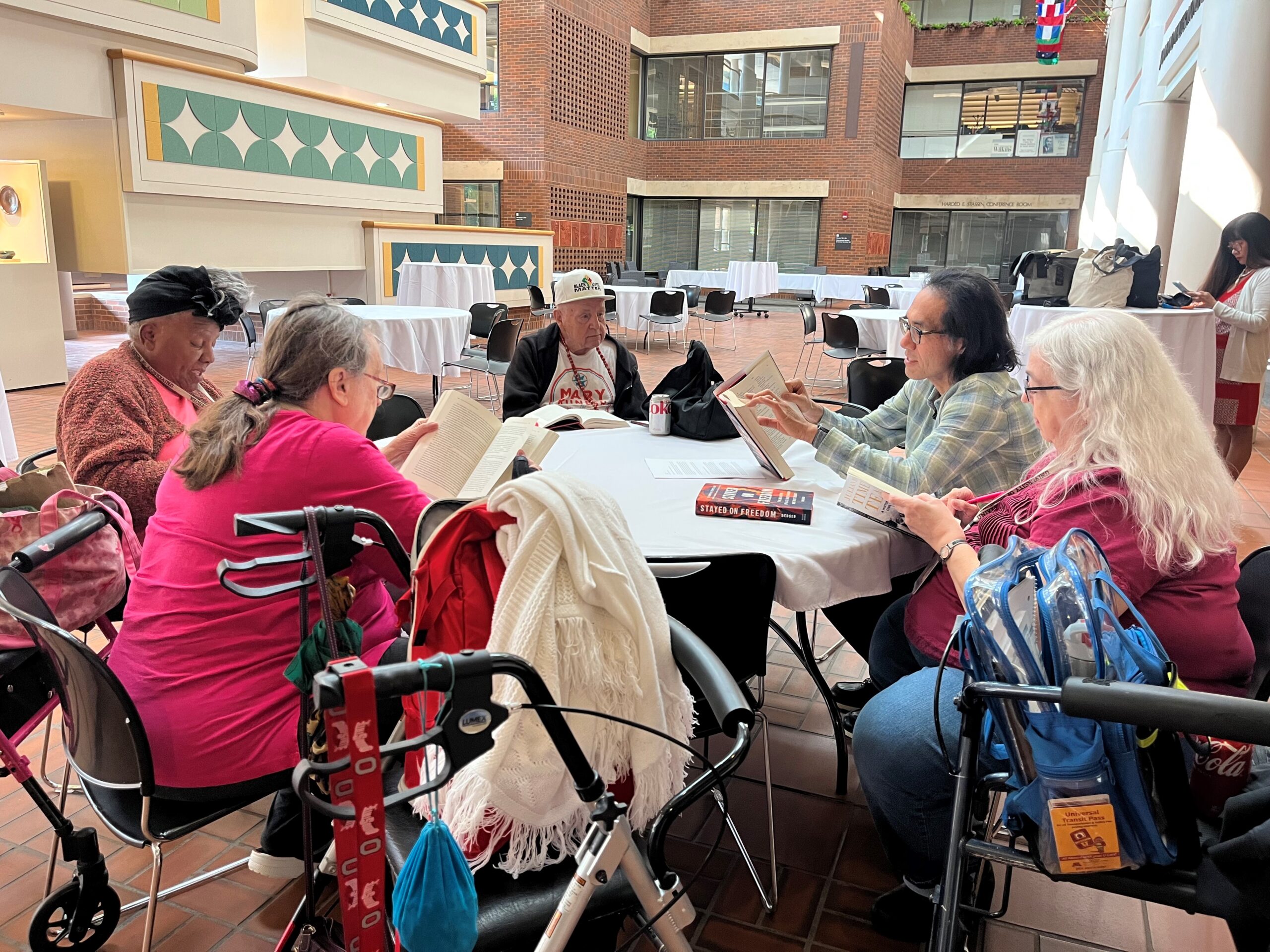 Aeon Affordable Homes Five older adults sit around a table reading books together in a bright, open space during the Summer of Learning.