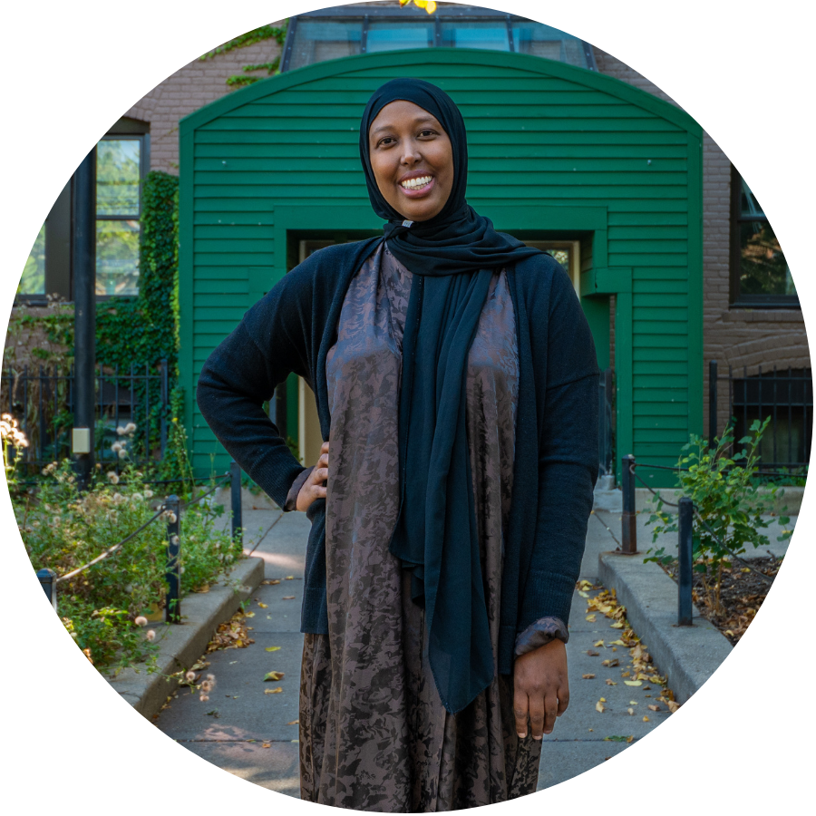 Aeon Affordable Homes A woman in a hijab smiles outside, standing before a green building at the Aeon MADACS 2025 event.
