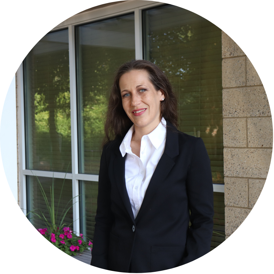 Aeon Affordable Homes Woman in a black blazer stands and smiles by a window with flowers outside, radiating Aeon elegance at MADACS 2025.