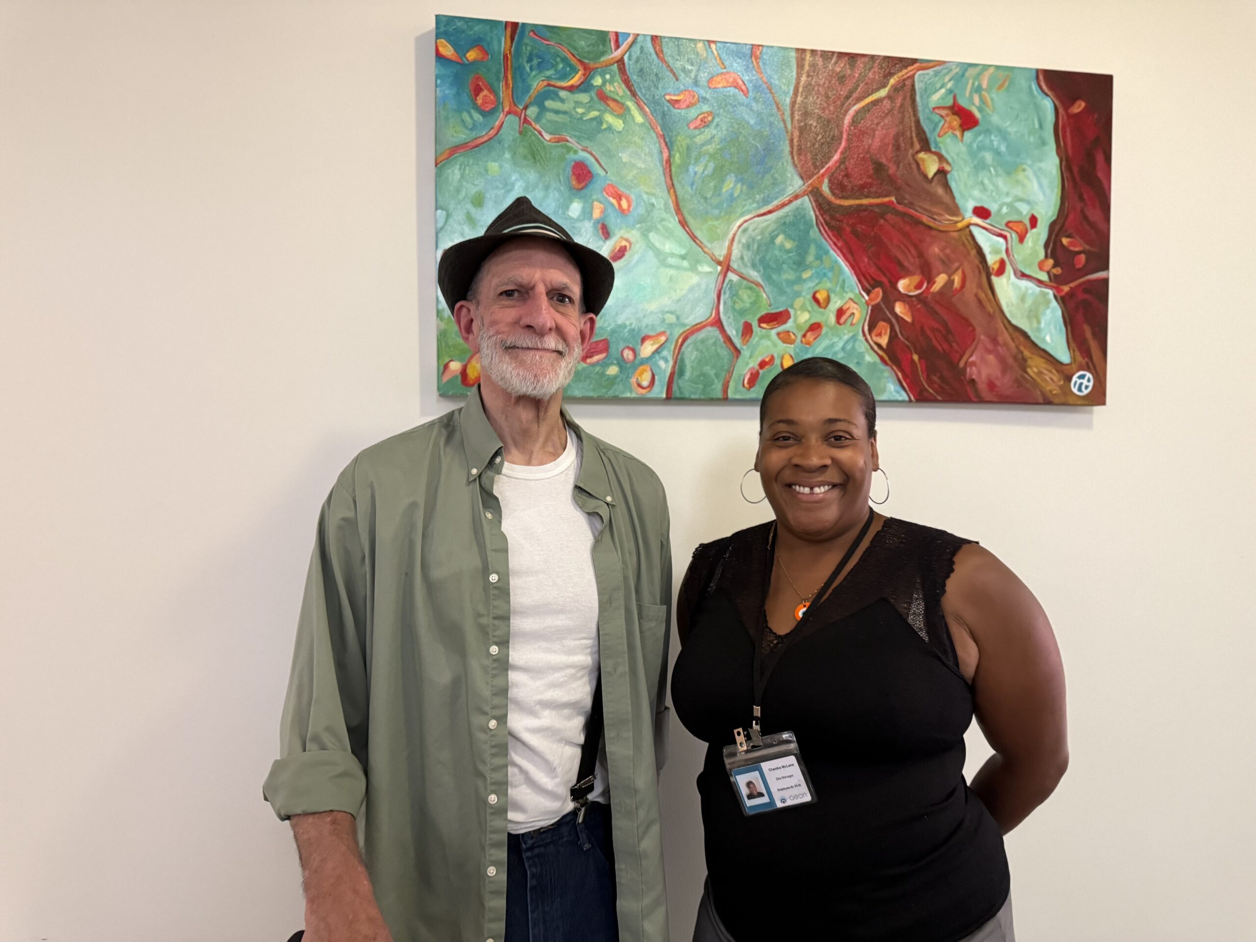 Aeon Affordable Homes Two people smiling and standing in front of a colorful abstract painting on a wall.