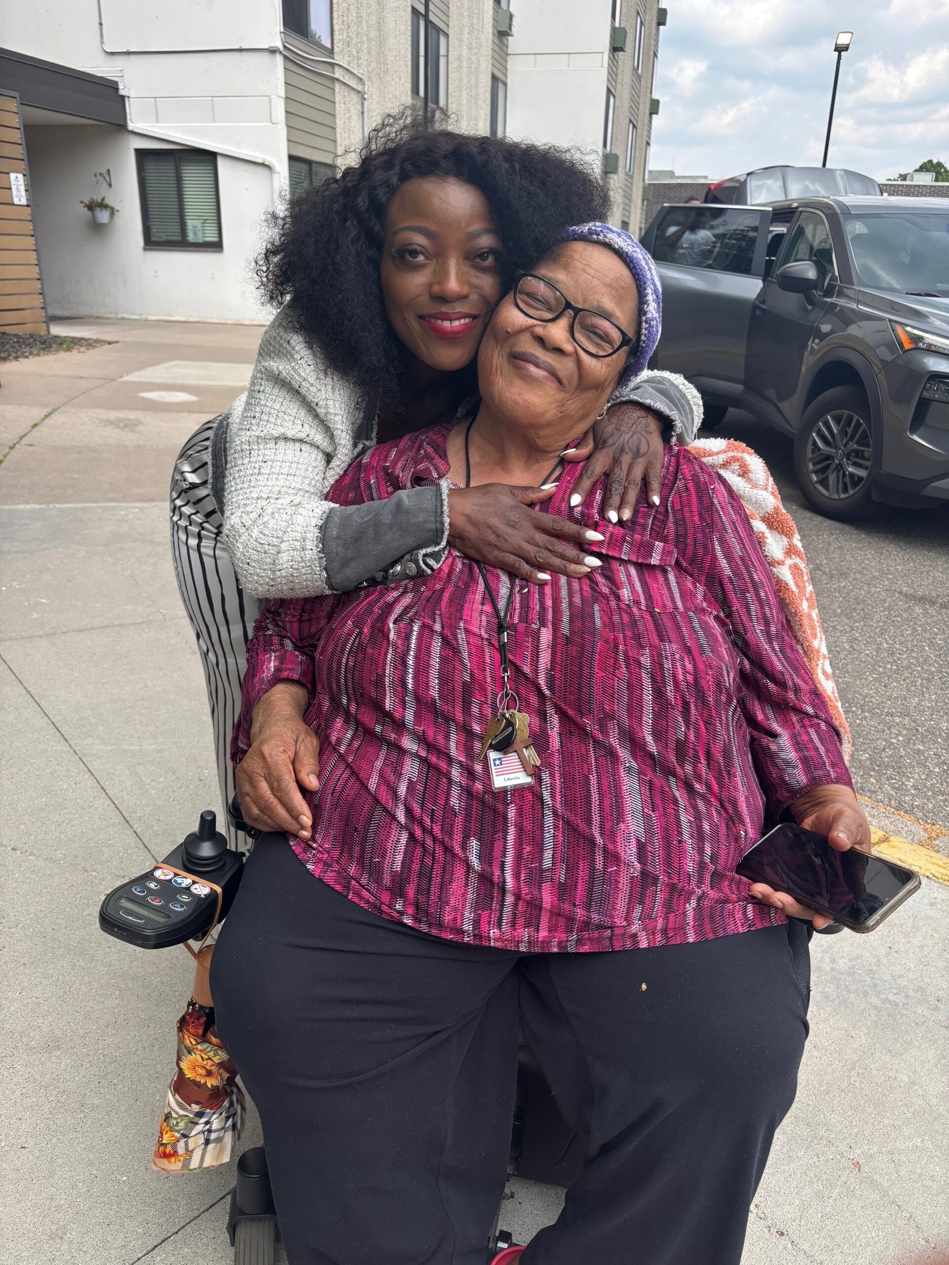Aeon Affordable Homes A woman hugs Ms. Kumba, who is seated in a power wheelchair.